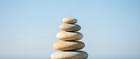 Balanced stack of smooth river stones creating zen meditation tower against soft blue sky background for wellness and mindfulness concepts.