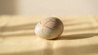 Cracked eggshell with natural brown speckled pattern resting on warm wooden surface with soft lighting and shallow depth of field for organic design concepts.