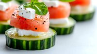 Fresh cucumber rounds topped with feta cheese and watermelon, garnished with basil leaves and black pepper, served as elegant appetizers on white background.