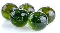 Glossy green glass marbles with bubbles inside arranged on white background, creating reflective surfaces and transparent depth effects.