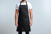 Caucasian male chef wearing black bib apron with white t-shirt against neutral gray background, professional culinary uniform for restaurant staff.