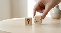 Hand placing wooden blocks with question mark and speech bubble symbols on table representing communication and problem-solving concepts.