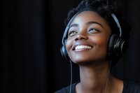 Young African American woman wearing headphones smiling with eyes closed while listening to music against dark background, expressing joy and relaxation.