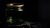 Glowing glass jar with golden lid on dark textured surface, emitting soft green light from within, suitable for mystical, fantasy, and magical themed designs.