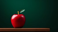 Fresh red apple with green leaf on wooden surface against dark green background. Minimalist food photography with dramatic lighting and copy space.