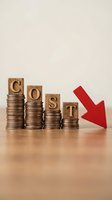 Decreasing coin stacks with wooden blocks spelling COST and red arrow pointing down showing expense reduction and budget optimization concept.