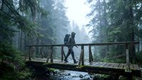 Couple hiking across wooden bridge in misty forest with evergreen trees and stream below, outdoor adventure and nature exploration.