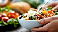 Fresh quinoa bowl with roasted vegetables, cherry tomatoes, and leafy greens garnished with herbs, served in white ceramic bowl, healthy meal concept.
