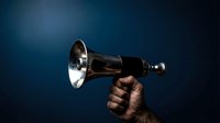Hand holding vintage brass bell against dark blue background for announcements and communication concepts.