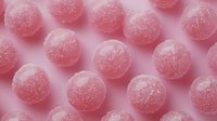 Pink sugar-coated spheres with crystalline texture arranged on soft pink background. Candy confectionery design element for packaging, advertising, and sweet treats marketing.