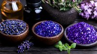 Aromatic lavender spa composition with dried flowers, bath salt crystals in wooden bowls, essential oils and fresh herbs on dark background.