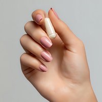 Female hand with elegant pink manicure holding white pill or supplement capsule against neutral gray background, demonstrating medication intake.
