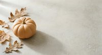 Golden pumpkin with dried autumn leaves on neutral textured background for seasonal decoration and fall harvest themed designs.
