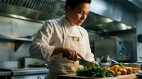 Professional male chef preparing fresh vegetables in modern commercial kitchen with stainless steel equipment for culinary food preparation and cooking.