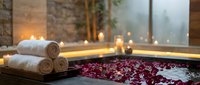 Luxury spa bathtub filled with rose petals and candles creating romantic wellness atmosphere for relaxation and self-care rituals.