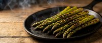 Grilled asparagus spears with herbs and seasoning on cast iron skillet, steaming hot vegetable side dish for healthy cooking and dining.