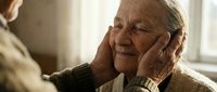 Senior man with gray hair and glasses receiving affectionate touch on face from another person, expressing warmth, care, and emotional connection in intimate moment.