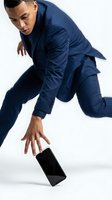 Young man of mixed ethnicity in navy business suit reaching down to catch falling smartphone against white background. Corporate professional.