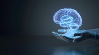 Glowing blue holographic brain floating above open palm against dark background representing artificial intelligence, neuroscience and mental health concepts.