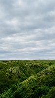 Lush green valley landscape with rolling hills covered in moss and vegetation under dramatic cloudy sky, suitable for nature and environmental design projects.