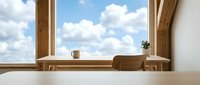 Wooden desk with cup and plant on windowsill overlooking blue sky with clouds, minimalist workspace interior design for office and home decor projects.