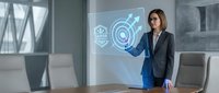 Professional businesswoman in dark suit interacting with futuristic holographic interface displaying digital icons in modern office conference room.
