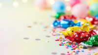 Colorful party decorations with shiny ribbons, confetti and festive elements scattered on light background for celebration events and holiday designs.