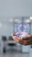 Hands holding glowing digital brain with neural network connections and data visualization in modern office environment, representing artificial intelligence, machine learning, and innovative technology solutions.