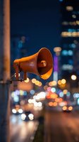 Orange megaphone speaker against blurred city lights at night creating bokeh effect for communication and announcement concepts.