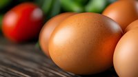 Fresh brown eggs on rustic wooden surface with colorful vegetables in background for healthy cooking and farm-to-table cuisine concepts.