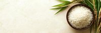 Raw white jasmine rice in wooden bowl with fresh green palm leaf on light stone background, top view with copy space for menu or recipe.