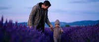 Adult male and young child in brown jackets standing together in expansive lavender field at dusk, mountains visible in background, suitable for family, parenting, nature and lifestyle content.