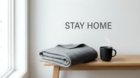 Cozy stay home concept with folded gray blanket and steaming black mug on wooden bench against white wall with text.