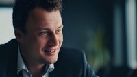 Confident Caucasian businessman in dark suit smiling during professional conversation in modern office environment.