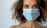 Young woman with intense blue eyes wearing protective medical face mask against white background, bare shoulders and wavy brown hair. Healthcare concept.