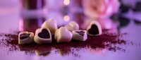 Heart-shaped chocolates and cocoa powder on purple surface with bokeh lights, romantic confectionery for Valentine's Day, love, and dessert designs.