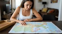 Young Hispanic woman planning travel route studying world map at home kitchen table for vacation destination research and trip preparation adventure.