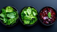 Fresh green spinach leaves and diced red beetroot in black ceramic bowls on dark background, healthy vegetarian ingredients for salad preparation.