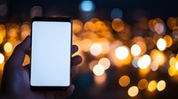 Hand holding smartphone with blank white screen against blurred golden bokeh lights background creating magical evening atmosphere.