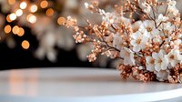 Delicate cherry blossom branches with soft pink and white flowers on elegant table surface with warm golden bokeh lights creating romantic spring atmosphere.
