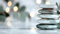 Stack of smooth gray zen stones balanced on white surface with soft bokeh lights creating peaceful spa atmosphere for meditation and wellness.