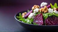 Fresh beet and goat cheese salad with arugula, walnuts on black plate against dark background. Healthy Mediterranean cuisine served restaurant style.