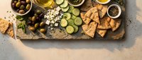 Mediterranean appetizer platter with olives, cheese, crackers and fresh vegetables on rustic wooden board for entertaining and social gatherings.