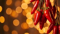 Red hot chili peppers hanging in bunch against warm golden bokeh lights background for culinary spice cooking ingredient kitchen decoration.