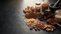 Cocoa powder, chocolate bars, nuts and spices arranged on dark surface for baking and confectionery preparation in rustic kitchen setting.