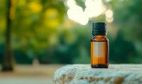 Small amber essential oil bottle on stone surface against blurred green natural background with bokeh lights, wellness and aromatherapy concept.
