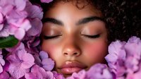 Young African American woman with closed eyes and natural curly hair surrounded by pink hydrangea flowers, expressing serenity and wellness in beauty portrait.
