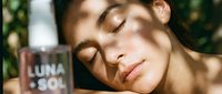 Young woman with medium skin tone relaxing outdoors in sunlight, eyes closed peacefully, holding beverage cup. Wellness and lifestyle concept for advertising, wellness brands, and lifestyle marketing.