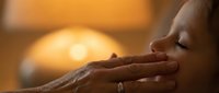 Young woman applying skincare cream with gentle hands in warm golden lighting for beauty and wellness routine.