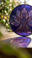 Purple stained glass meditation figure suncatcher hanging in sunlight with bokeh background creating peaceful spiritual atmosphere for mindfulness practice.